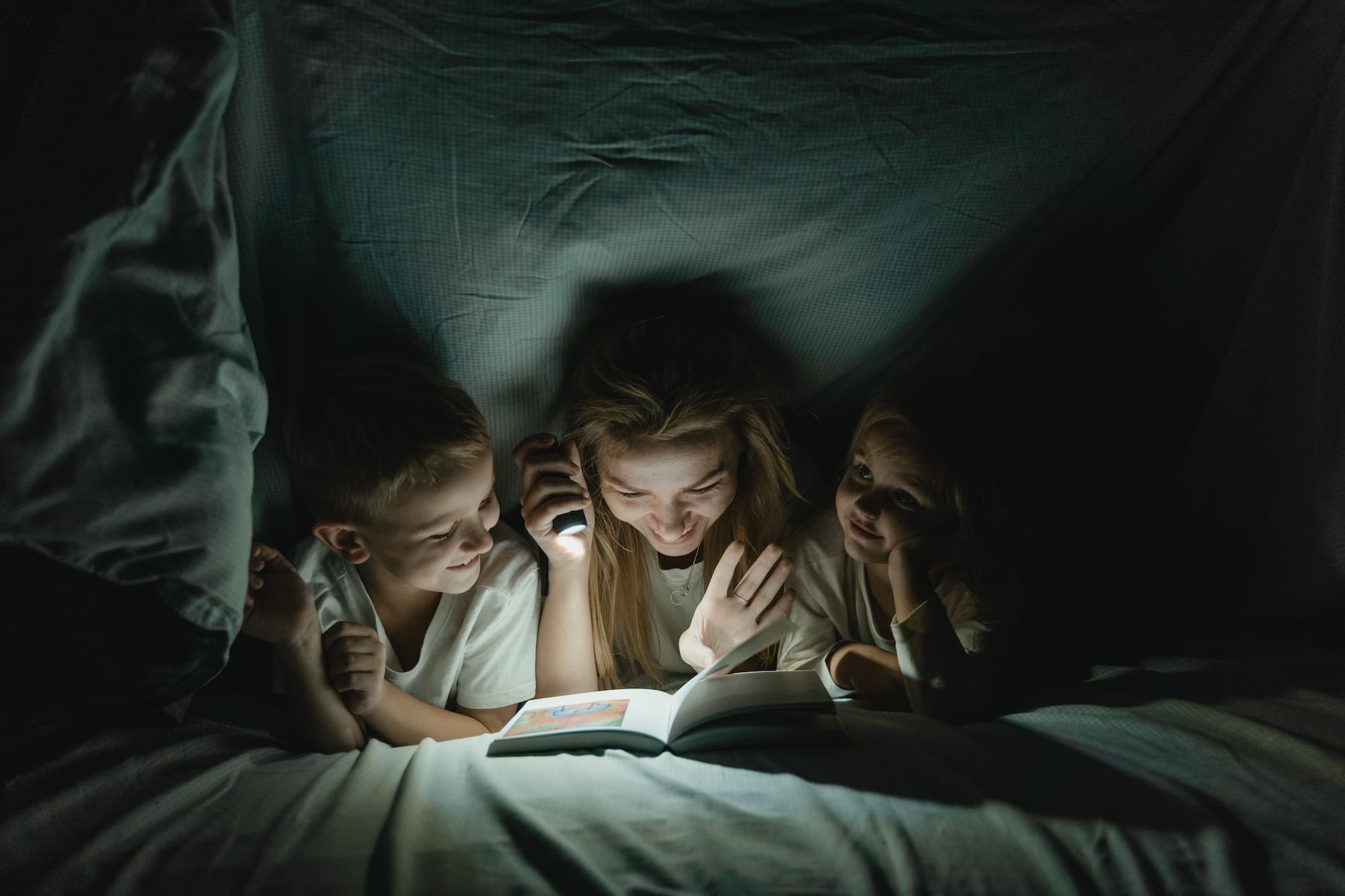 Mom reading a book with her kids under the covers, safe from bed bugs and other pests that cause health risk